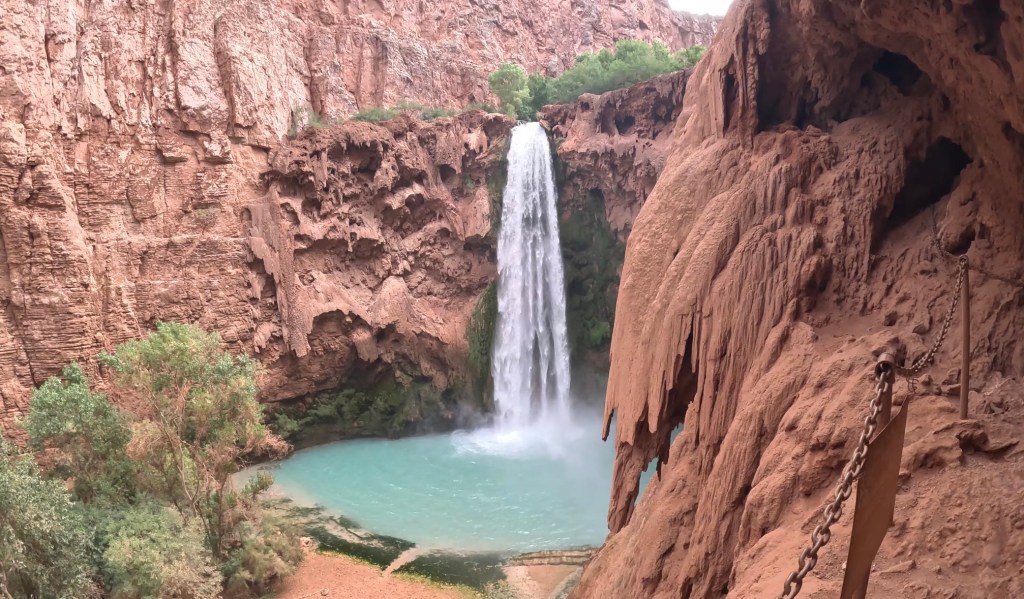 Large waterfall of teal blue water with cliffs all around. 